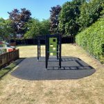 Side view of a Lappset multi-use climbing structure with grass mat surfacing and red boundary markings on a school field.