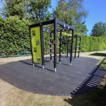 Lappset climbing frame installed on grass mats in a fenced school playground with hedges and clear blue sky.